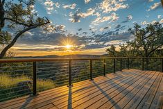 the sun is setting over a wooden deck with railings and trees in the foreground