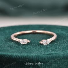 a rose gold ring with two pear shaped diamonds on it, sitting on top of a green velvet box