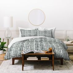 a white bed with black and white comforter in a room next to a table