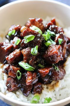 a white bowl filled with rice and meat on top of a blue table cloth next to chopsticks