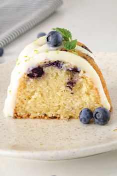 a slice of blueberry cake on a plate with white frosting and fresh blueberries