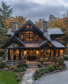 a large house with lots of windows and lights on it's front porch, surrounded by trees