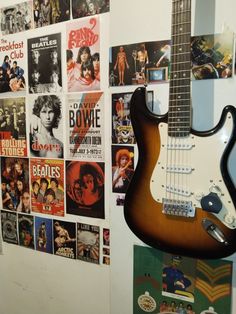 an electric guitar hanging on the wall next to a bunch of pictures and posters behind it