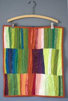 a multicolored quilt hanging on a wall next to a hanger with clothes pins