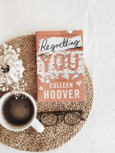 a cup of coffee next to a book titled regeting you by collien hoover