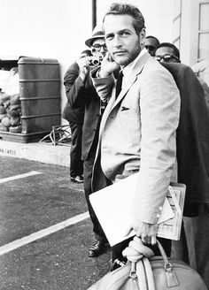 a black and white photo of a man in a suit walking down the street while holding a camera