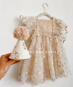 a hand holding a small white party hat next to a dress on a hanger