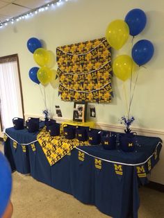 a table topped with blue and yellow balloons next to a wall hanging on the wall