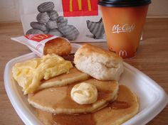 a plate with pancakes, butter and syrup on it next to a cup of coffee