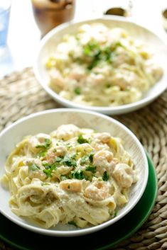 two white plates filled with pasta and shrimp on top of a green plate next to a glass of water