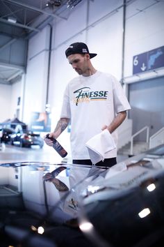 a man standing next to a car in a garage holding a bottle and paper towel