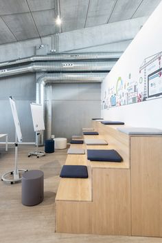 an empty room with wooden benches and stools on the floor in front of a white wall