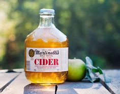 a bottle of cider sitting on top of a wooden table next to an apple