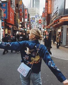 a woman holding her arms out in the air while walking down a busy city street