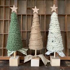 three small christmas trees are on display in front of a wooden box with twine