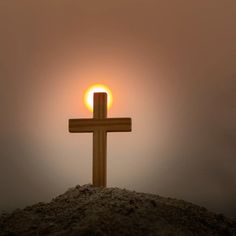 a cross on top of a hill with the sun in the sky behind it and foggy background