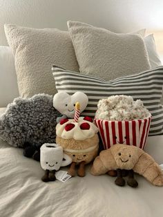 stuffed animals are sitting on a bed with popcorn and cakes in front of the pillows