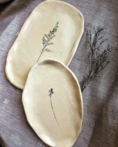 two white plates with plants on them sitting on a cloth covered tablecloth next to each other