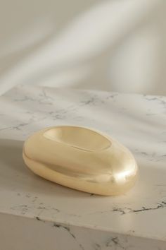 a white marble table with a gold object on it's side and a light colored background