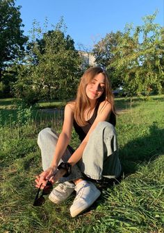 a woman sitting in the grass with her shoes on and one hand resting on her knee