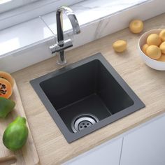 a kitchen sink sitting on top of a counter next to a bowl of oranges