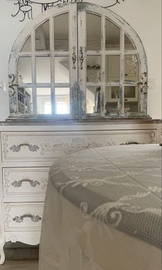 a white dresser with an ornate mirror above it and a bed in the foreground