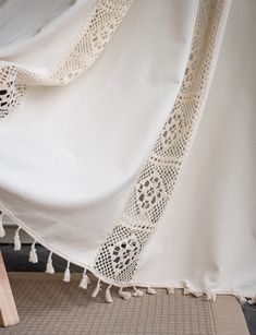 a white table cloth with tassels on it sitting next to a wooden chair