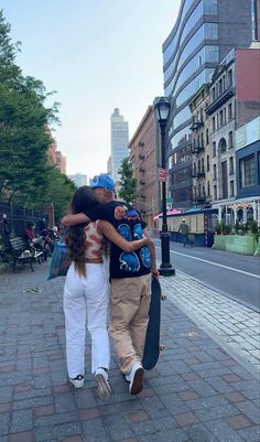 two people walking down the street with their arms around each other and one person holding a skateboard