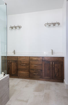 a large bathroom with two sinks and wooden cabinetry on the wall, along with a glass shower door