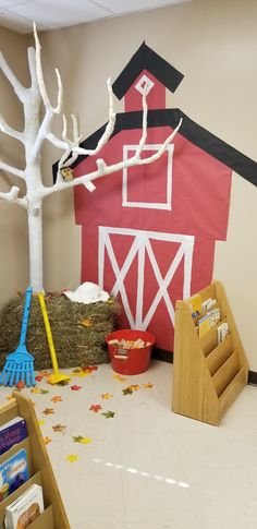 a red barn with hay and brooms on the floor next to a white tree