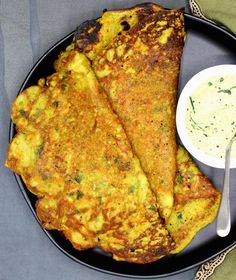 two omelets on a black plate with a bowl of sauce