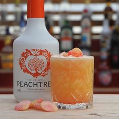 an orange drink sitting on top of a table next to a bottle and some candies