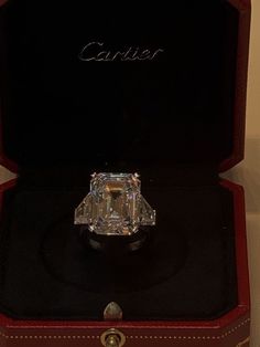 a fancy diamond ring sitting in a red case on top of a black box with the word cartier written above it