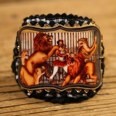 a ring with an image of lions and men in cages on the front, sitting on a wooden surface