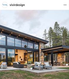 a modern house with glass walls and lots of furniture on the lawn outside at dusk