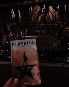 someone holding up a playbill book in front of a stage