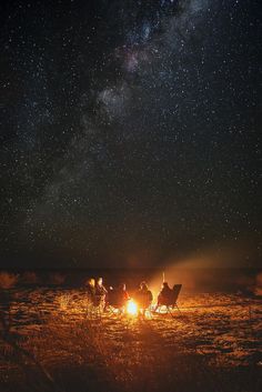 people sitting around a campfire under the night sky