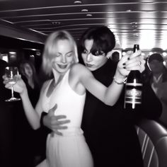 two women dressed in black and white pose for a photo while holding wineglasses