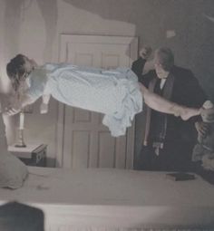 a woman in a blue dress is jumping on a bed while two men look on