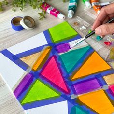 someone is painting an art project with colored paper and watercolors on the table