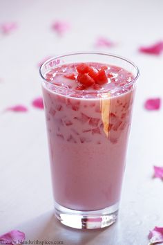 there is a drink with strawberries in it on the table next to rose petals