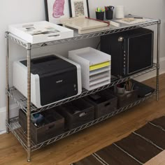 a metal shelf with two computers and printer's on it in front of a wall