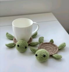 two crocheted sea turtle coasters and a coffee cup on a white table