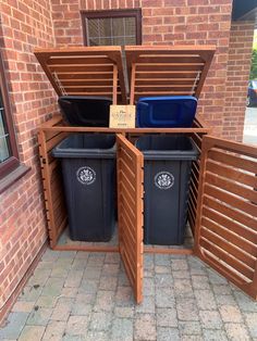 two trash cans are in the middle of an open wooden box on the side of a brick building