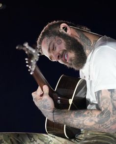 a man with tattoos playing an acoustic guitar