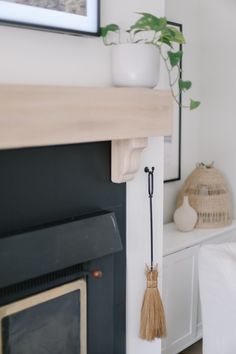 a fireplace with a potted plant on top of it and a broom hanging from the mantle