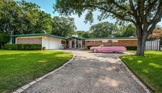 a pink car is parked in front of a house with trees and grass around it