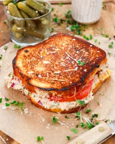 a grilled cheese sandwich with tomatoes and green olives on a wooden cutting board