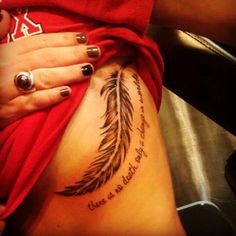 a woman's stomach with a feather tattoo on the side and words written in cursive writing