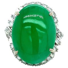 A 14 karat white gold ring that features one cabochon apple green jade gauged at 22.0 mm x 16.32 mm at its center. It is accented by a halo of thirty round full-cut and baguette-cut diamonds, totaling approximately 1.00 carat (graded H-I color and SI clarity). Stamped: 585. Total weight: 14.0 grams. Size 5.75. Vintage Cocktail Ring, Jade Ring, Baguette Cut Diamond, White Gold Ring, Apple Green, Green Jade, Gem Stone, Jade Green, Cocktail Rings